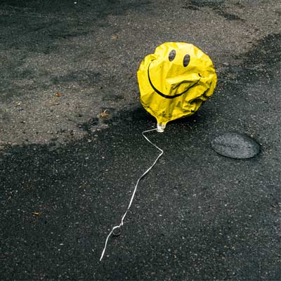 Ein Luftballon mit einem Smiley Aufdruck hat fast seine Luft verloren und liegt auf der Straße.
