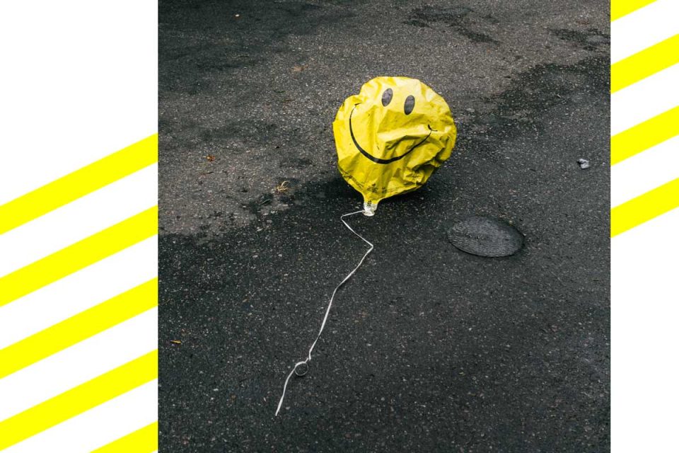 Ein zerknitterter Ballon mit Smiley-Aufdruck liegt auf dem Straßenasphalt.